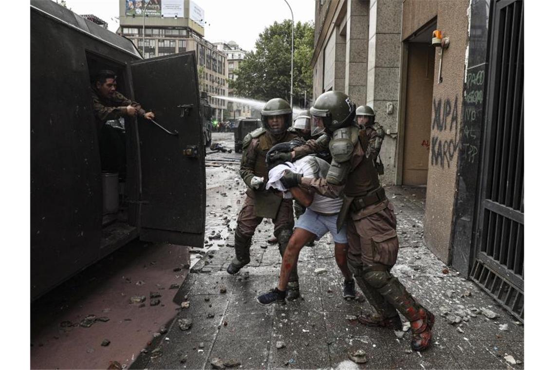 75.000 Chilenen protestieren gegen soziale Ungleichheit Polizisten verhaften einen Demonstranten: Die gewalttätigen Ausschreitungen in Chile nehmen kein Ende. Foto: Esteban Felix/AP/dpa
