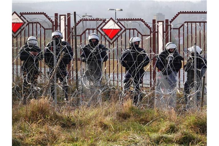 Polnische Sicherheitskräfte stehen an der Grenze hinter Stacheldraht. Foto: Ulf Mauder/dpa