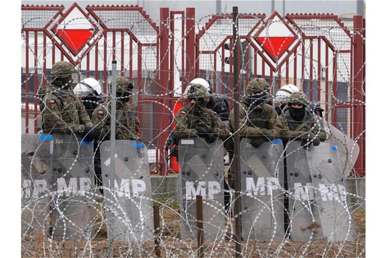Polnische Sicherheitskräfte stehen hinter dem Grenzzaun am Grenzübergang Brusgi (Belarus) und Kuznica (Polen). Foto: Ulf Mauder/dpa