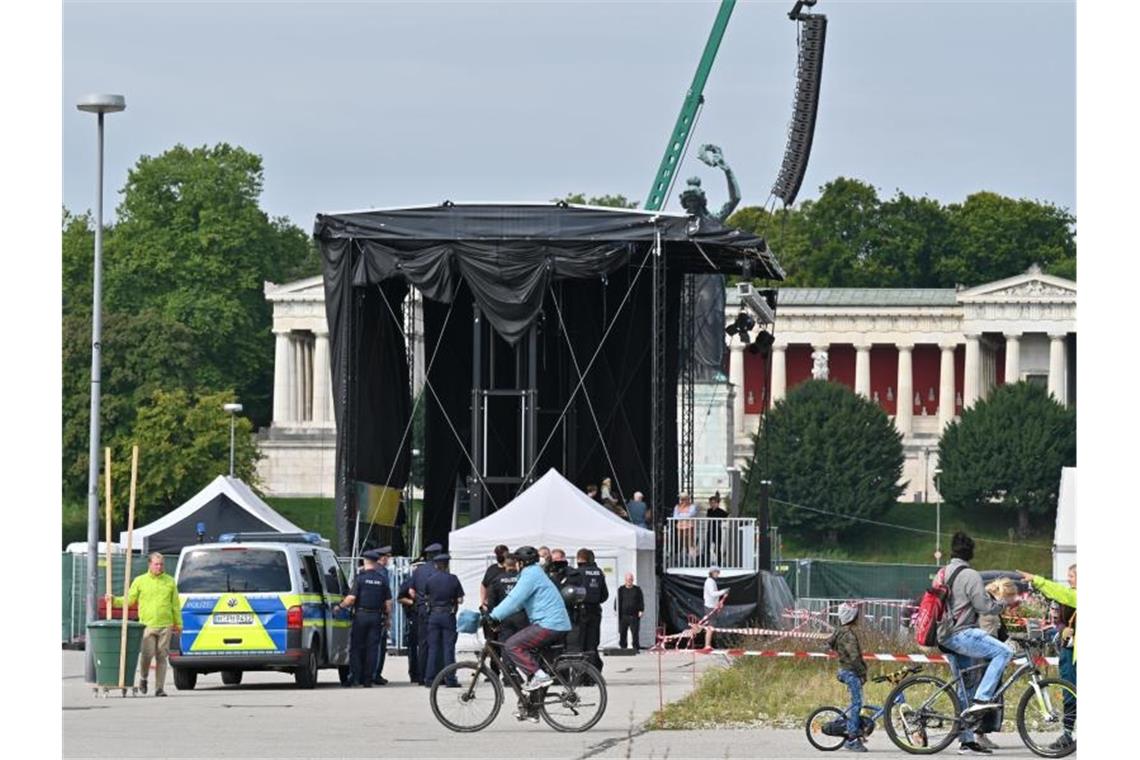 Radler fahren über die Theresienwiese, während im Hintergrund Polizisten vor der Bühne stehen. Unter dem Motto „#aussteigen“ finden eine Demonstration und eine Fahrradsternfahrt gegen die Internationale Automobil Ausstellung (IAA) statt. Foto: Felix Kästle/dpa