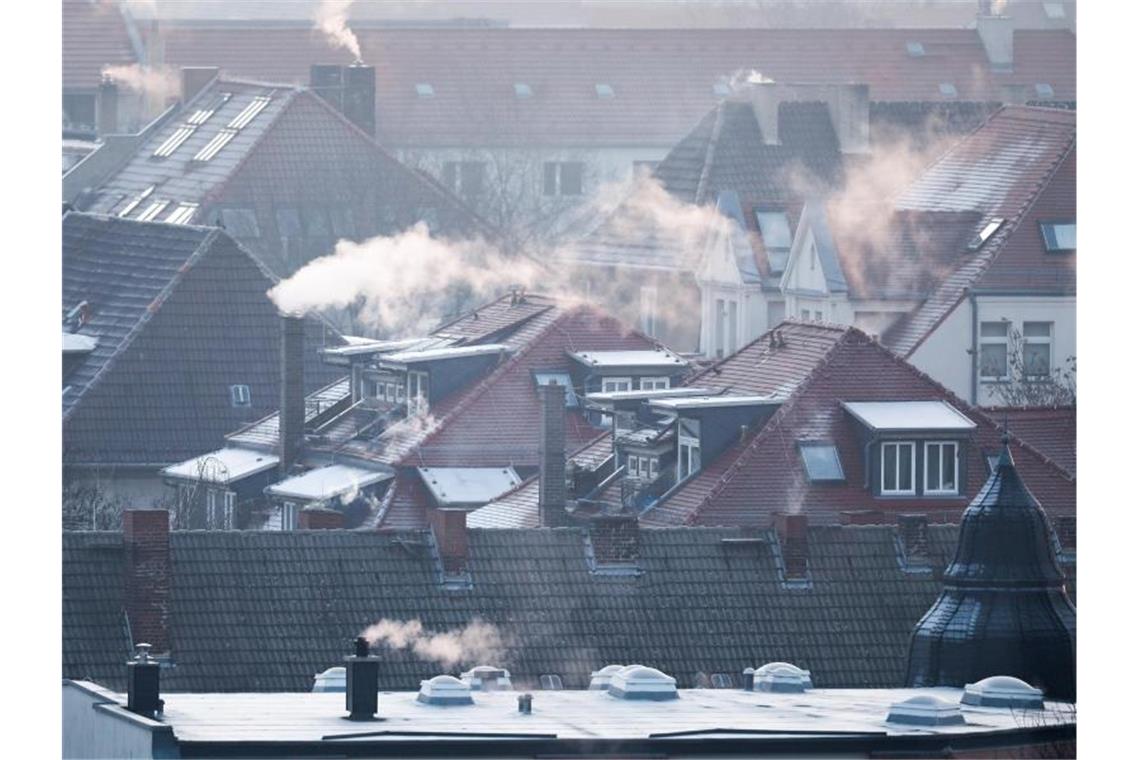 Rauch steigt aus den Kaminen auf den Dächern von Mehrfamilienhäusern an einem kalten Wintermorgen. Foto: Jan Woitas/dpa