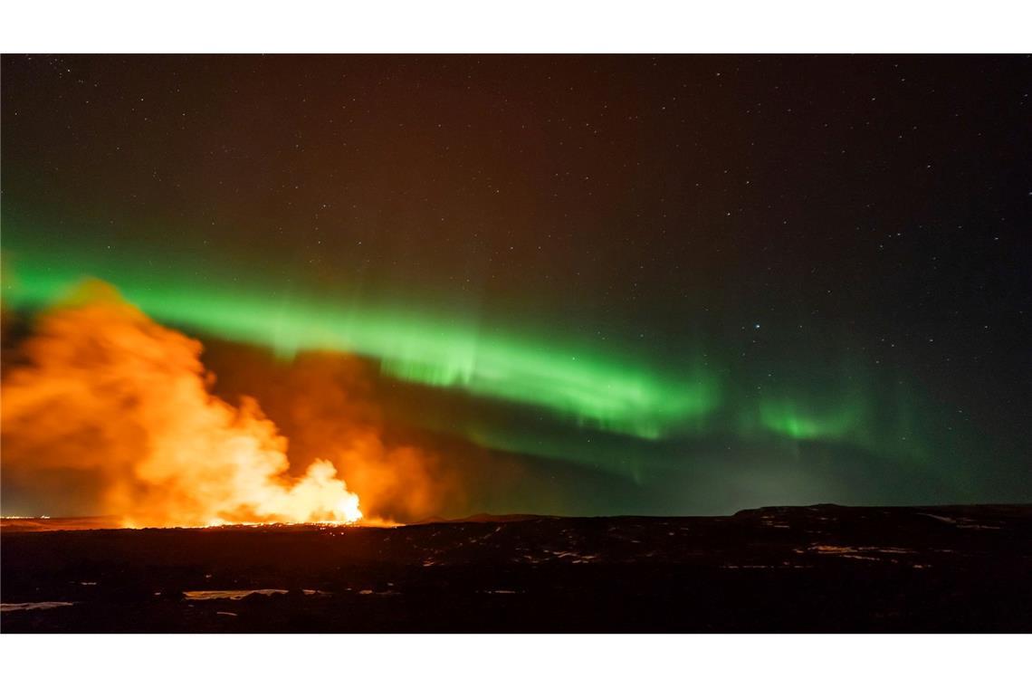 Rauch steigt vom Ausbruchsgebiet eines Vulkans im Südwesten Islands auf, während Polarlichter am Himmel erscheinen.