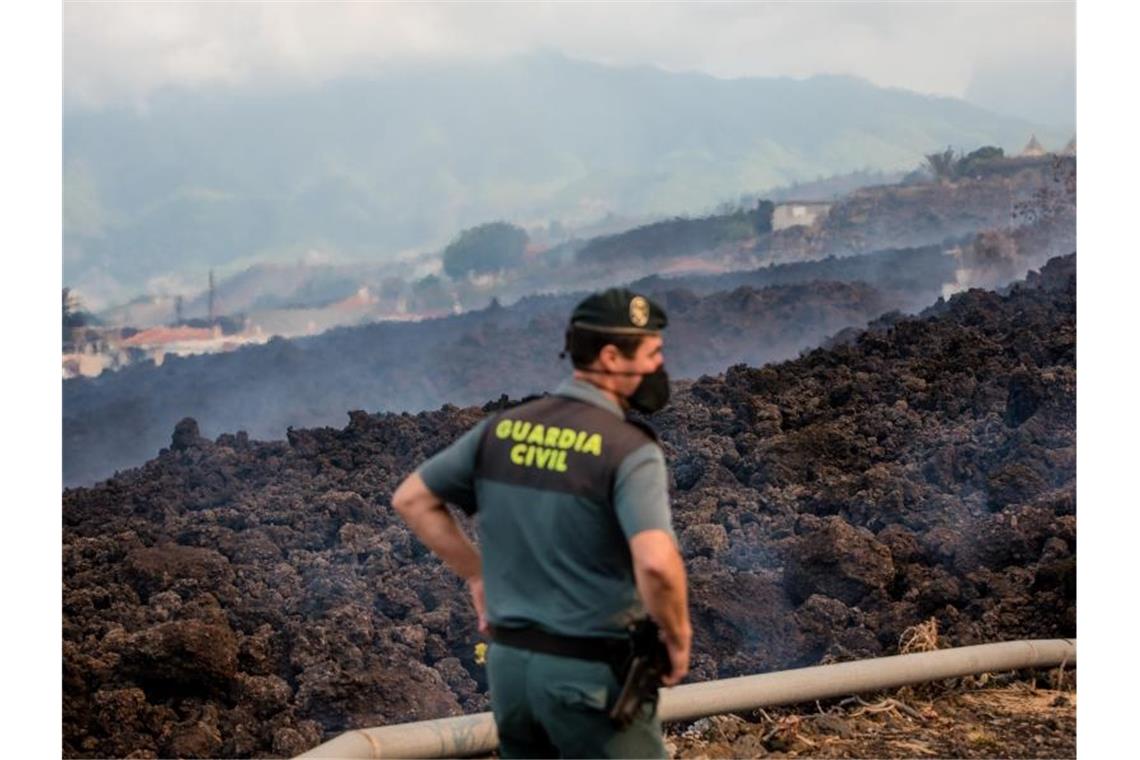 Vulkanausbruch auf Kanaren: Tausende Menschen auf der Flucht Rauch steigt vor einem Beamten der Guardia Civil von abkühlender Lava auf, die über eine Straße geflossen ist. Foto: Arturo Jiménez/dpa