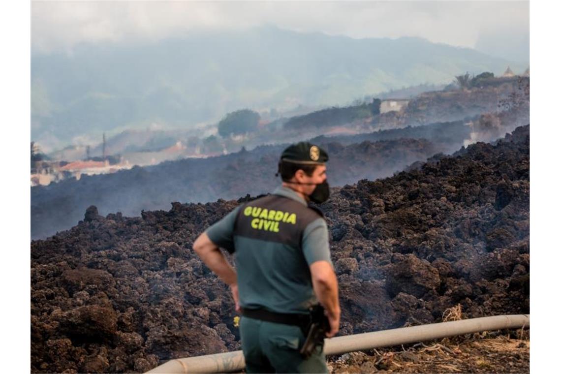 Rauch steigt vor einem Beamten der Guardia Civil von abkühlender Lava auf, die über eine Straße geflossen ist. Foto: Arturo Jiménez/dpa