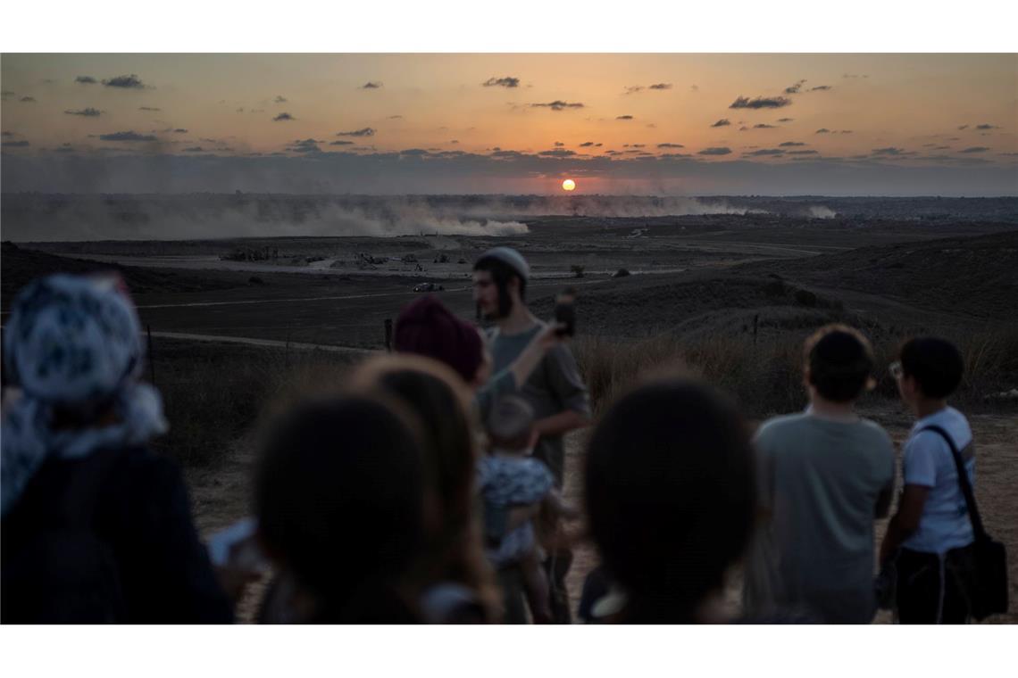 Bilder des Tages Rechtsgerichtete israelische Siedler versammeln sich an der Grenze zum Gazastreifen, während im Hintergrund Rauchschwaden von vorrückenden israelischen Panzern zu sehen sind.