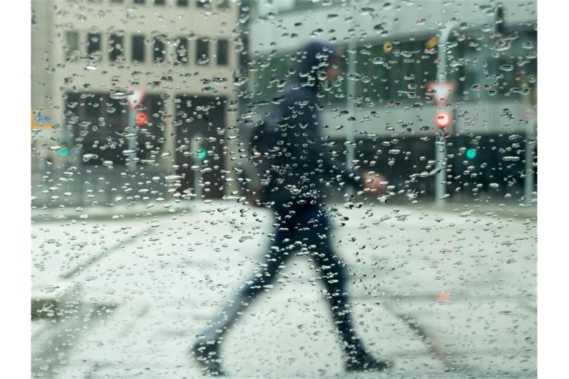 Nach dem Sturm ist vor dem Sturm: Warnungen vor Unwettern Regentropfen sammeln sich auf einer Autscheibe an der ein Mann vorbeigeht. Foto: Bernd Weißbrod/dpa/Archivbild