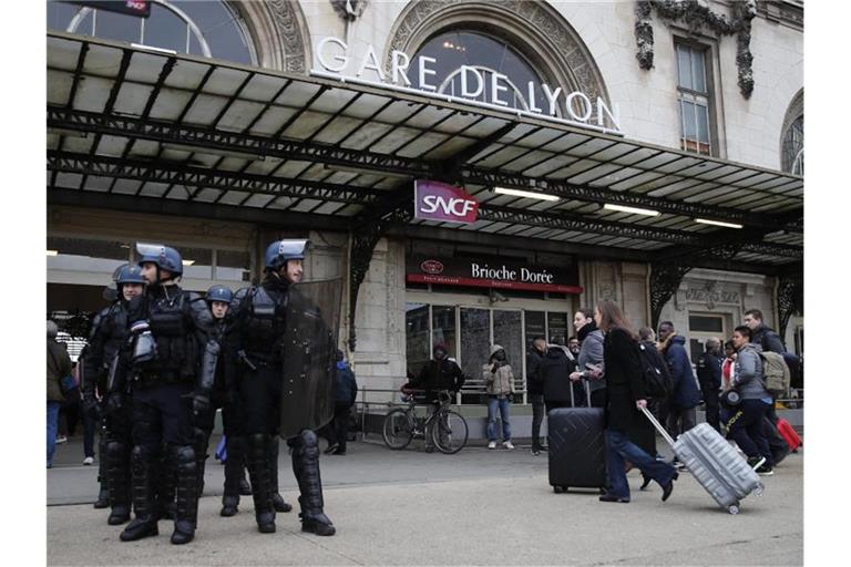 Reisende am Gare de Lyon, der während einer Demonstration der streikenden Eisenbahner von Polizisten bewacht wird. Foto: Francois Mori/AP/dpa