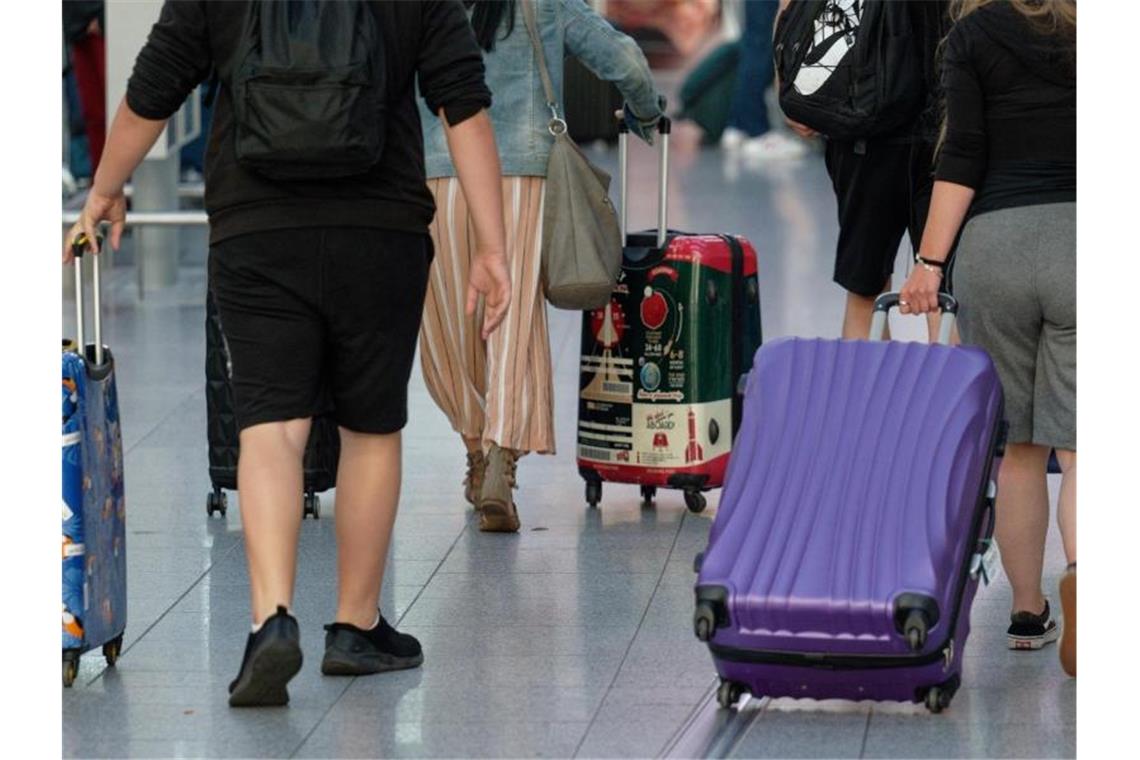 Reisende gehen mit Koffern durch die Abflughalle eines Flughafens. Foto: Henning Kaiser/dpa/Symbolbild