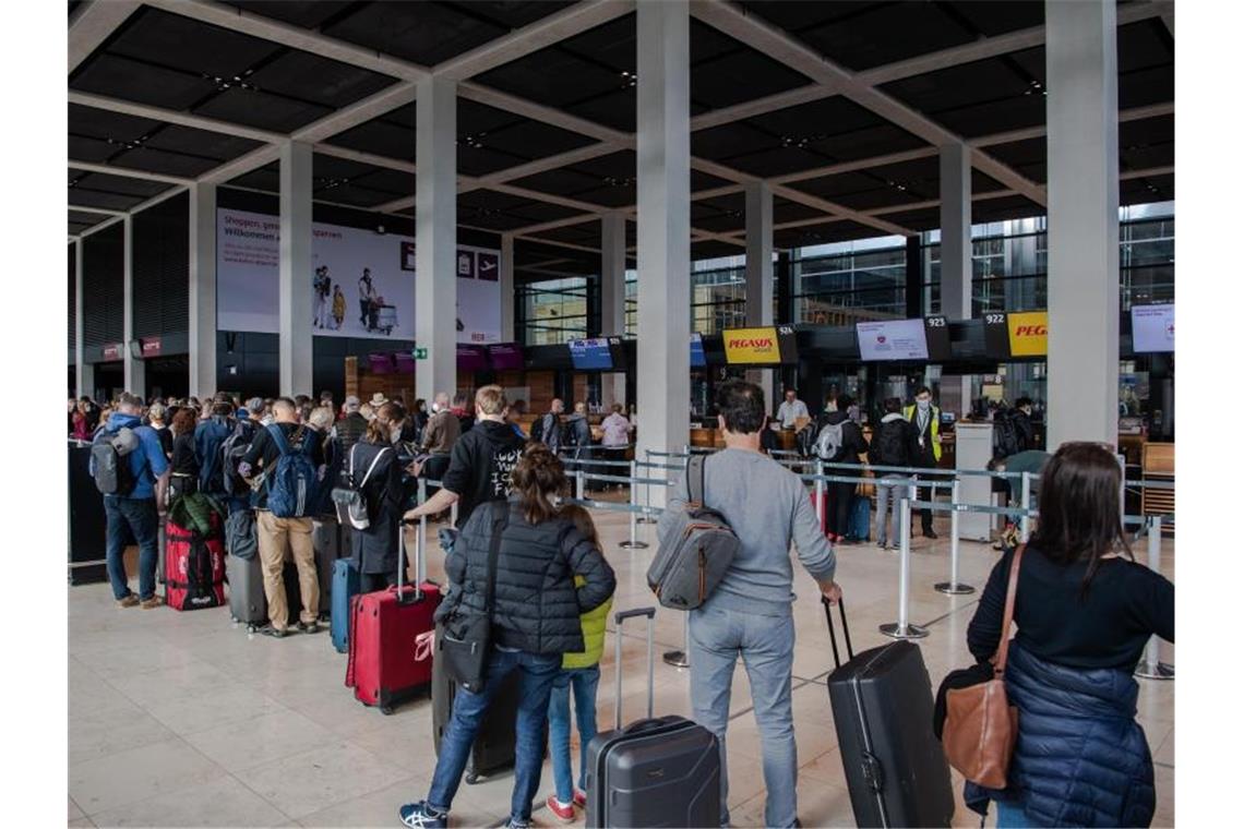 Reisende stehen am Flughafen BER vor einem Check-in-Schalter. Corona-Regeln beschränken weiterhin das freie Reisen. Foto: Paul Zinken/dpa