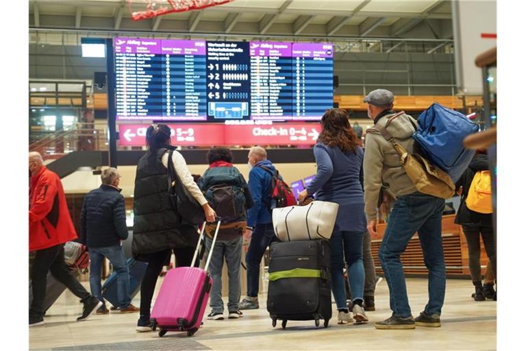 Reisende stehen am Flughafen BER vor einer Info-Tafel. Foto: Joerg Carstensen/dpa