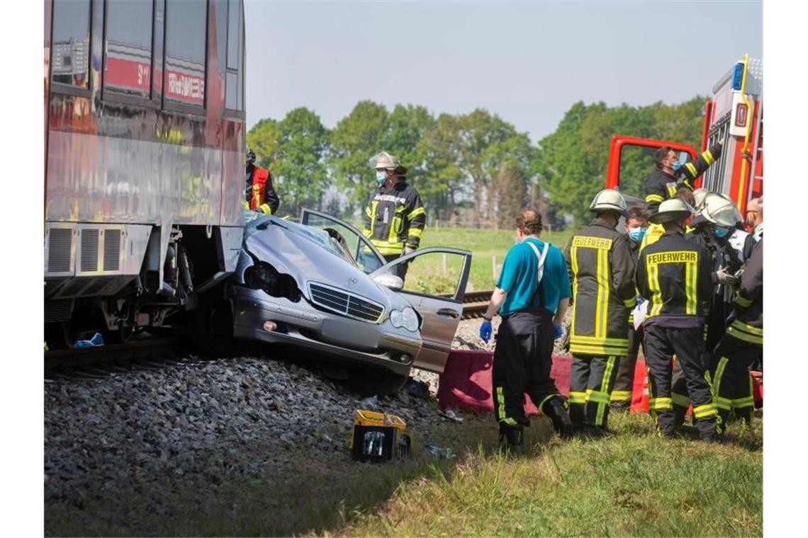 Rettungskräfte stehen an der Unfallstelle. Das Auto wurde von dem Zug etwa 50 Meter mitgeschleift. Foto: Arnulf Stoffel/dpa