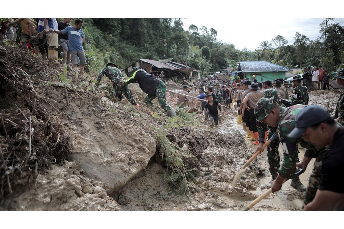 Rettungskräfte und Dorfbewohner beseitigen Schlamm.