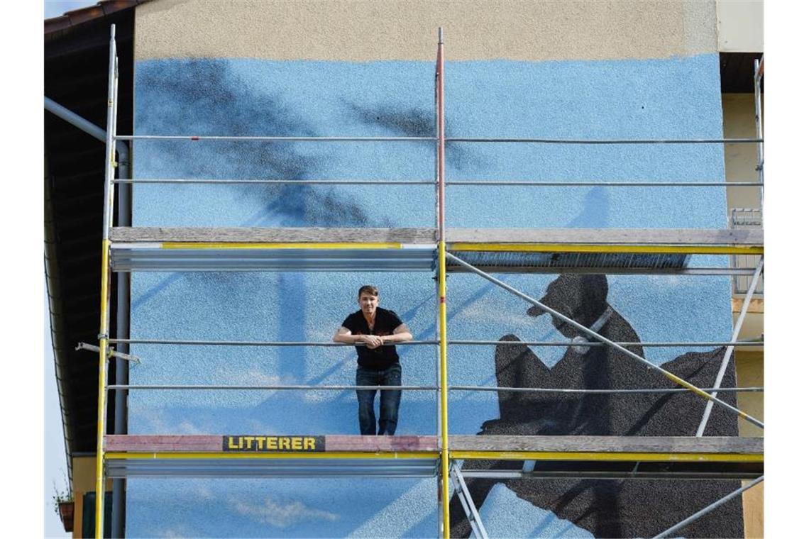 Mannheim: Wandbilder sollen Zusammenhalt im Quartier stärken Riojas steht im Stadtteil Schönau auf einem Gerüst vor einer Hausfassade mit einem seiner Wandbilder. Foto: Uwe Anspach/dpa