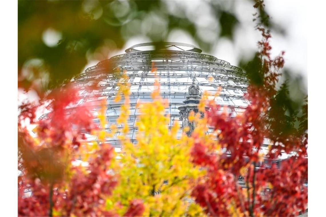 Rot-gelb-grün herbstlich verfärbte Blätter sind an Bäumen vor der Reichstagskuppel zu sehen. Foto: Britta Pedersen/dpa-Zentralbild/dpa