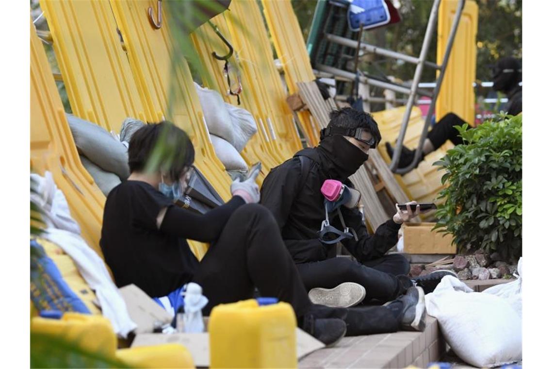 Ruhepause hinter einer Barrikade: Vermummte Demonstranten nach heftigen Auseinandersetzungen mit der Polizei vor der Polytechnischen Universität. Foto: -/kyodo/dpa