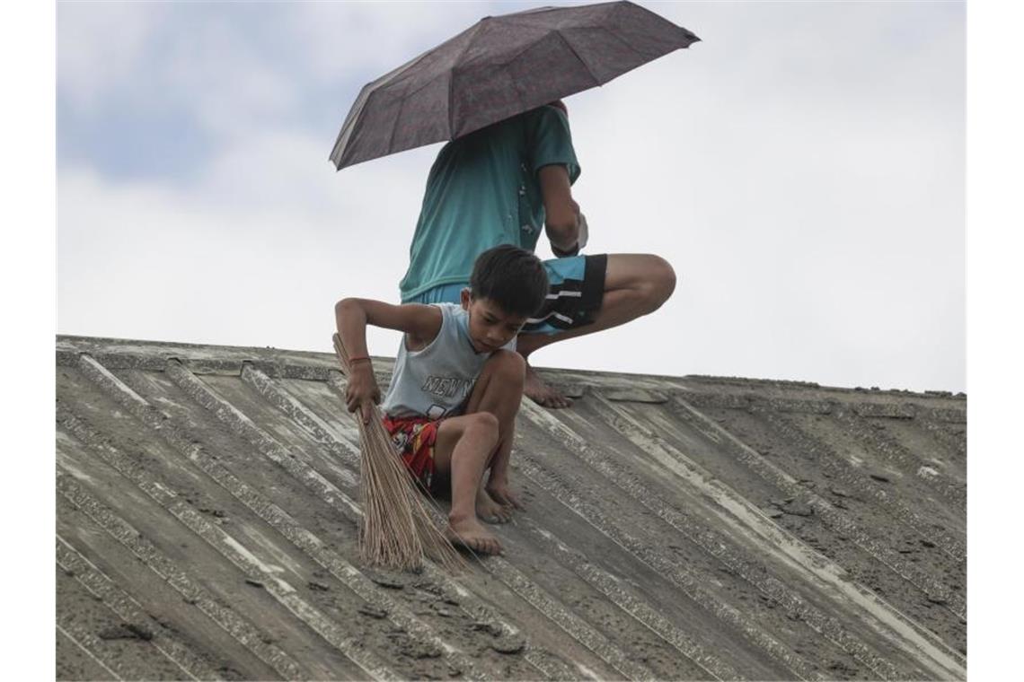 Saubermachen: Ein Junge hilft seiner Familie dabei, Vulkanasche vom Dach ihres Hauses in der Provinz Batangas zu entfernen. Foto: Aaron Favila/AP/dpa