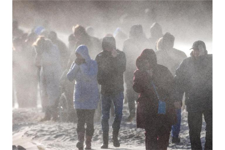 Schaulustige gehen durch den Sandsturm auf die Mole von Warnemünde. Urlauber und Tagesgäste beobachten bei Sonnenschein und kräftigem Wind den Wellengang durch das Sturmtief „Nadia“. Foto: Jens Büttner/dpa-Zentralbild/dpa