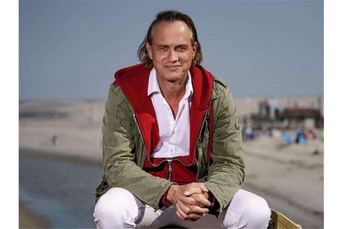 Bauers erster Film über das Surfen und den Tibet-Konflikt Schauspieler und Filmemacher Ralf Bauer sitzt am Strand von St. Peter Ording in der Sonne. Foto: Axel Heimken/dpa/Archivbild