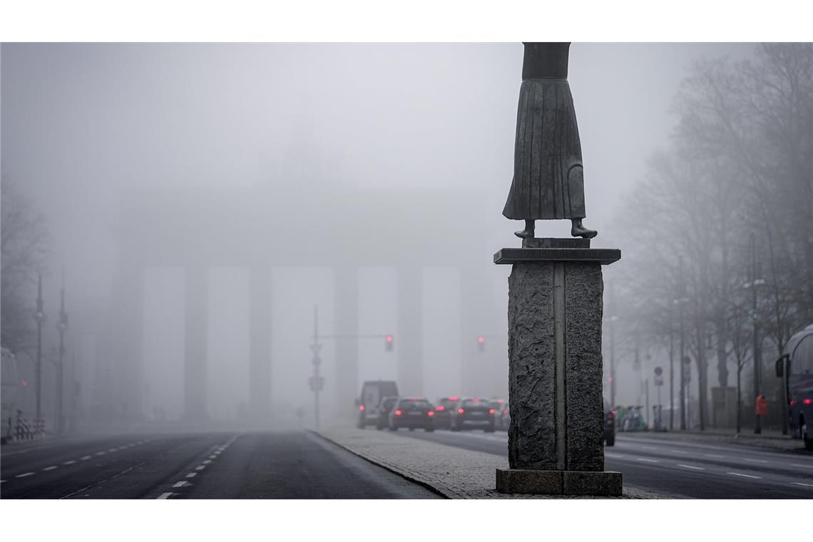 Schemenhaft ist das Brandenburger Tor im Nebel im Hintergrund der Bronzefigur "Der Rufer" von Gerhard Marcks am frühen Morgen zu sehen.