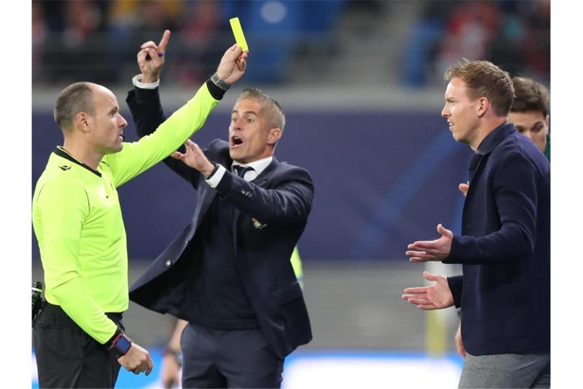 Schiedsrichter Antonio Mateu Lahoz (l) zeigt Leipzigs Trainer Julian Nagelsmann (r) die Gelbe Karte, dahinter gestikuliert Lyons Trainer Sylvinho. Foto: Jan Woitas/dpa-Zentralbild/dpa