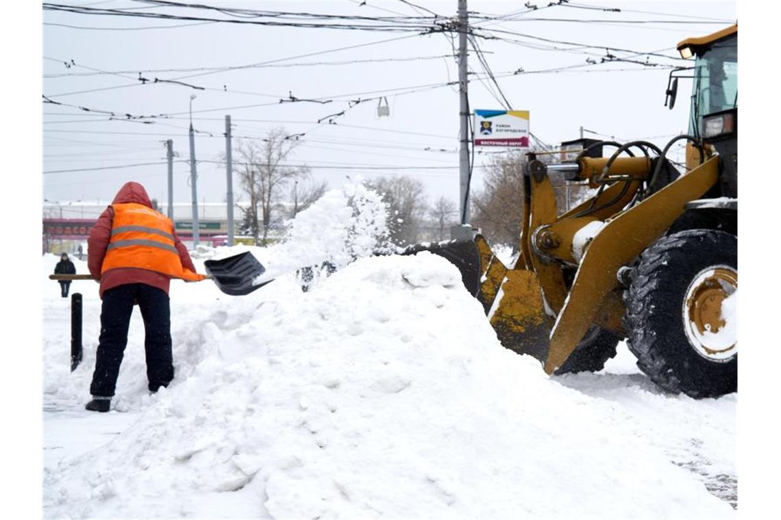 Moskau steuert auf Schneerekord zu Schnee wegräumen mit schwerem Gerät: Ein Mann schippt Schnee in die Schaufel eines Baggers. Foto: Mihail Tokmakov/SOPA Images via ZUMA Wire/dpa