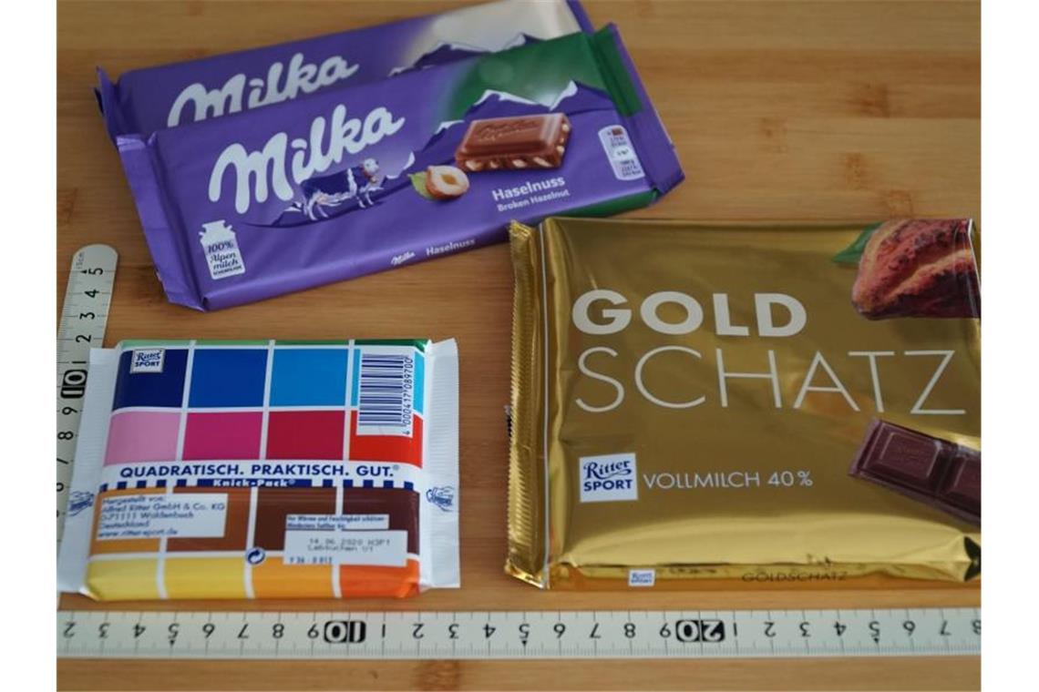 Schokoladentafeln der Marken Ritter Sport und Milka liegen neben einem Maßstab auf einem Tisch. Foto: Alexander Blum/dpa