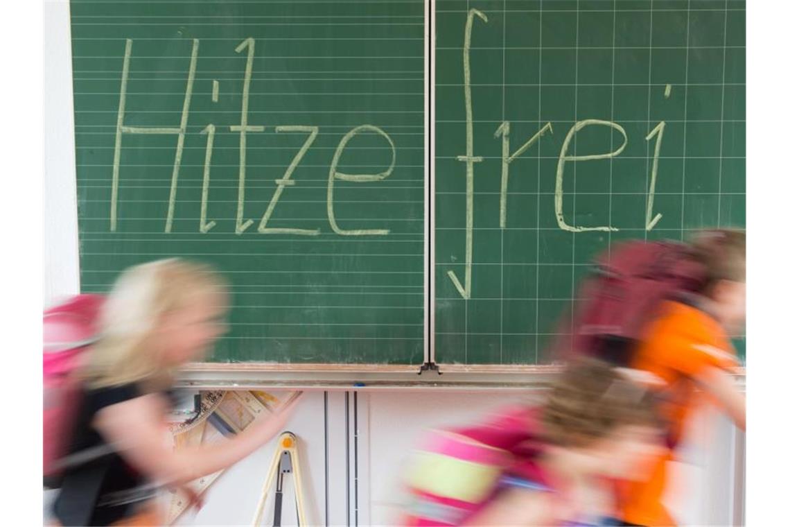 Schüler einer 2. Klasse laufen in einer Grundschule an einer Tafel mit der Aufschrift "Hitzefrei" vorbei. Foto: Sebastian Kahnert/Archivbild