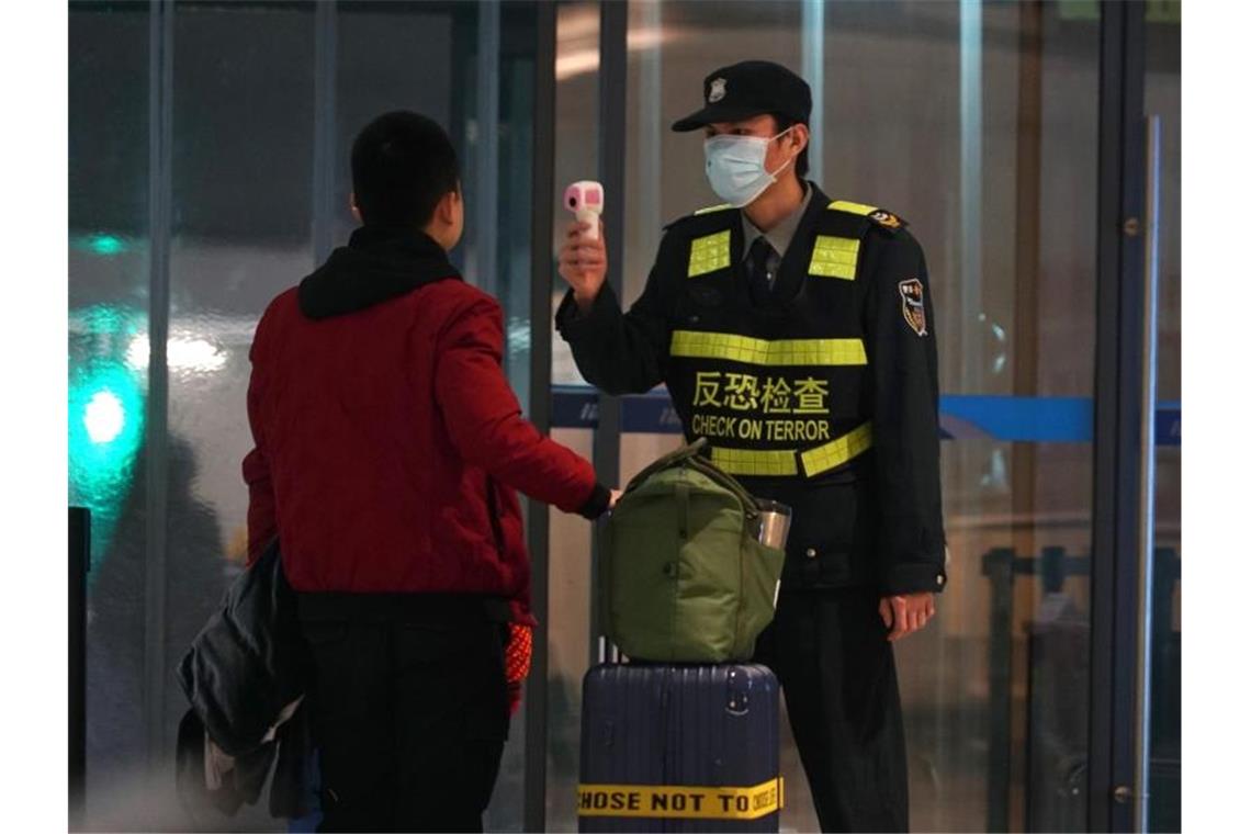 Neues Virus in China: Erster Fall in USA nachgewiesen Schutzmaßnahme gegen die Verbreitung des Corona-Virus: Ein Beamter misst am Flughafen von Wuhan die Körpertemperatur von Reisenden. Foto: Dake Kang/AP/dpa