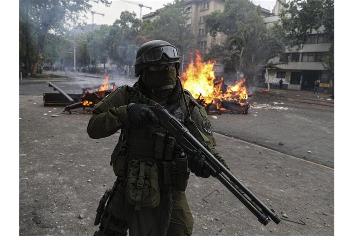 Schwer bewaffneter Polizist vor einer brennenden Straßensperre: Die gewalttätigen Proteste in Chile waren durch eine Erhöhung der Metro-Preise ausgelöst worden. Foto: Esteban Felix/AP/dpa