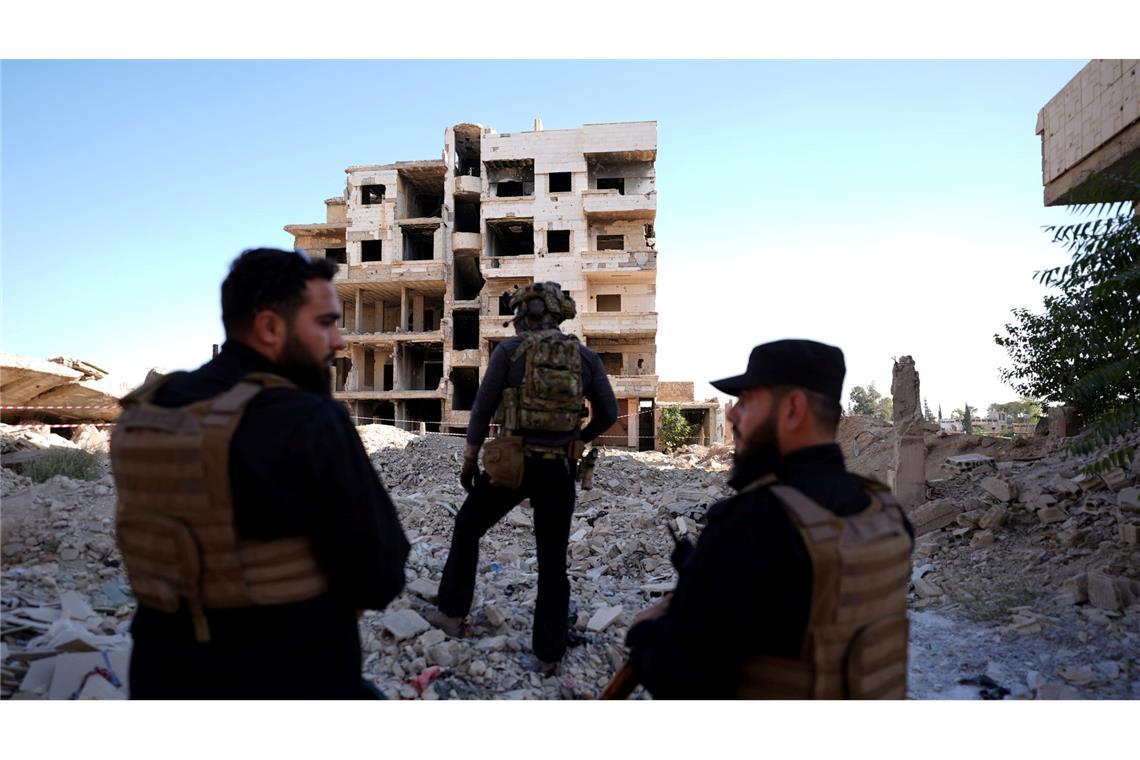 Sicherheitskräfte aus Syrien und aus Deutschland sichern den Besuch von Außenminister Wadephul bei einem humanitären Projekt in einer Straße mit während des Bürgerkriegs zerbombten Häusern in Harasta ab.