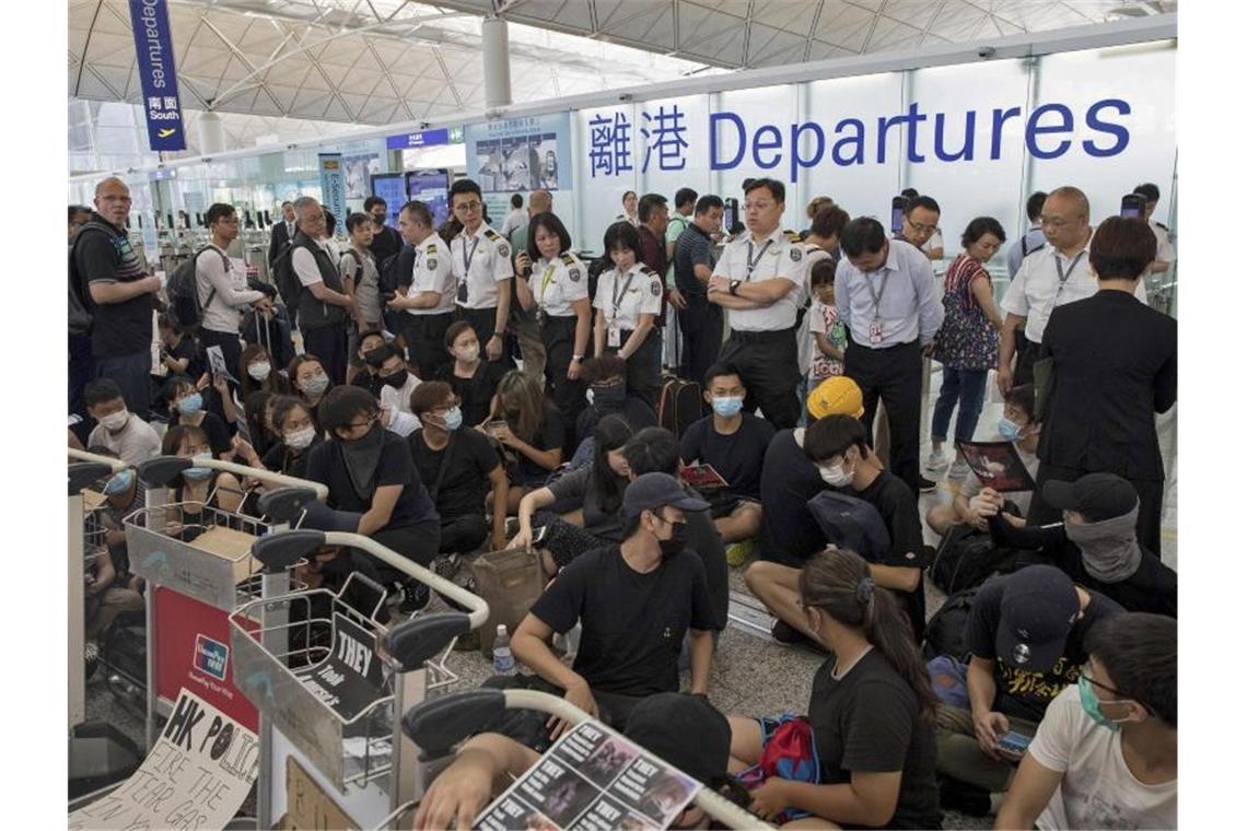 Heftige Zusammenstöße in Hongkongs Flughafen Sicherheitskräfte stehen hinter Demonstranten, die sich zu einem Sitzstreik im Terminal des Flughafens versammelt haben. Foto: Vincent Thian/AP