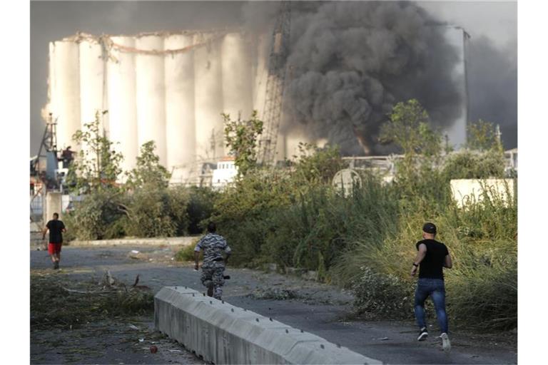 Sicherheitsleute laufen zum Ort der Explosion im Hafen von Beirut, während über dem Gebäude Rauch aufsteigt. Foto: Hussein Malla/AP/dpa