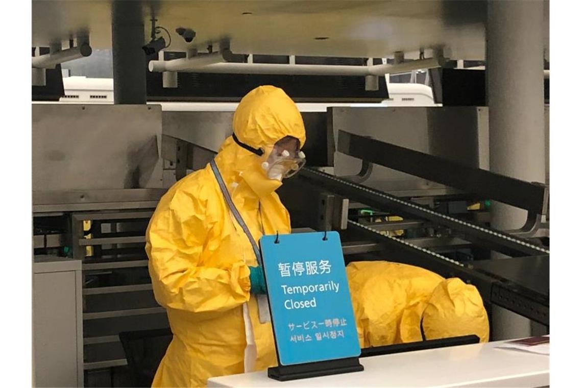 Sicherheitspersonal mit Schutzanzügen und Mundschutz steht hinter einem Schalter am Flughafen Wuhan. Foto: Lapresse/LaPresse via ZUMA Press/dpa