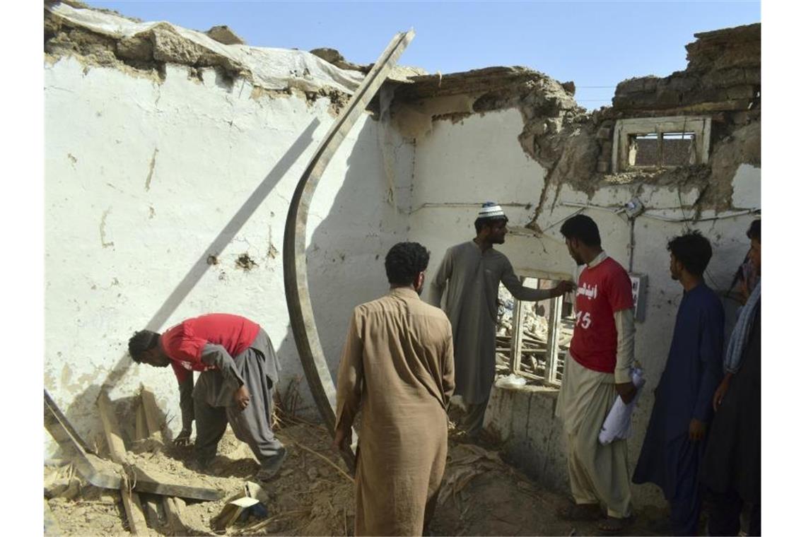 Sie suchen in einem zerstörten Haus nach Habseligkeiten!. Foto: Arshad Butt/AP/dpa