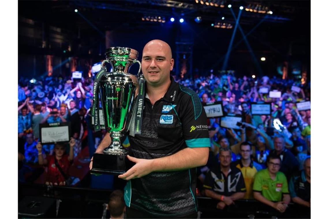 Unter Strom: Das wilde Auf und Ab von Darts-Elektriker Cross Sieger Rob Cross posiert mit dem Pokal. Foto: Swen Pförtner/dpa