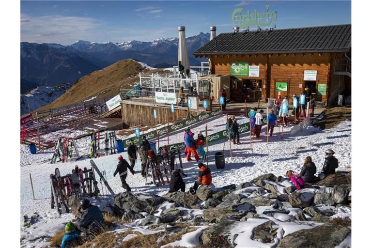 Skifahrer stehen auf einer Piste im Walliser Skigebiet vor einem Restaurant Schlange (Archivbild vom 28.11.2020). Foto: Jean-Christophe Bott/KEYSTONE/dpa