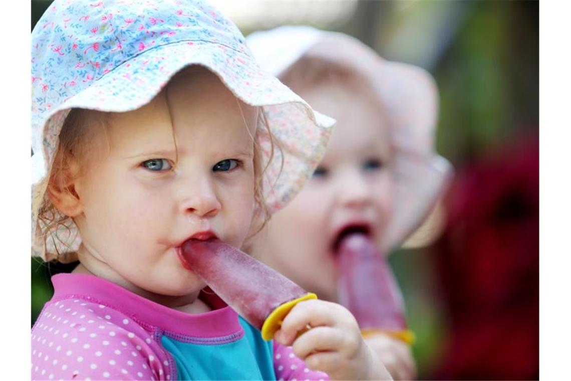 Hitze in Deutschland bringt möglicherweise Temperaturrekord So lässt es sich aushalten: Emma (l.) und Lotta, zwei Jahre alt, essen gut behütet im Schatten ein Eis. Foto: Roland Weihrauch