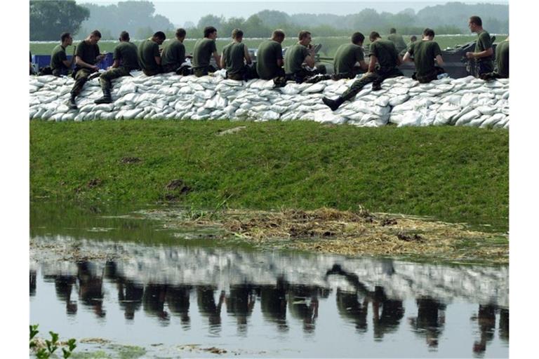 Soldaten spiegeln sich 2002 während der Mittagspause auf einem Deich bei Lauenburg im Wasser eines Seitenarms der Elbe. Foto: Kay_Nietfeld/dpa