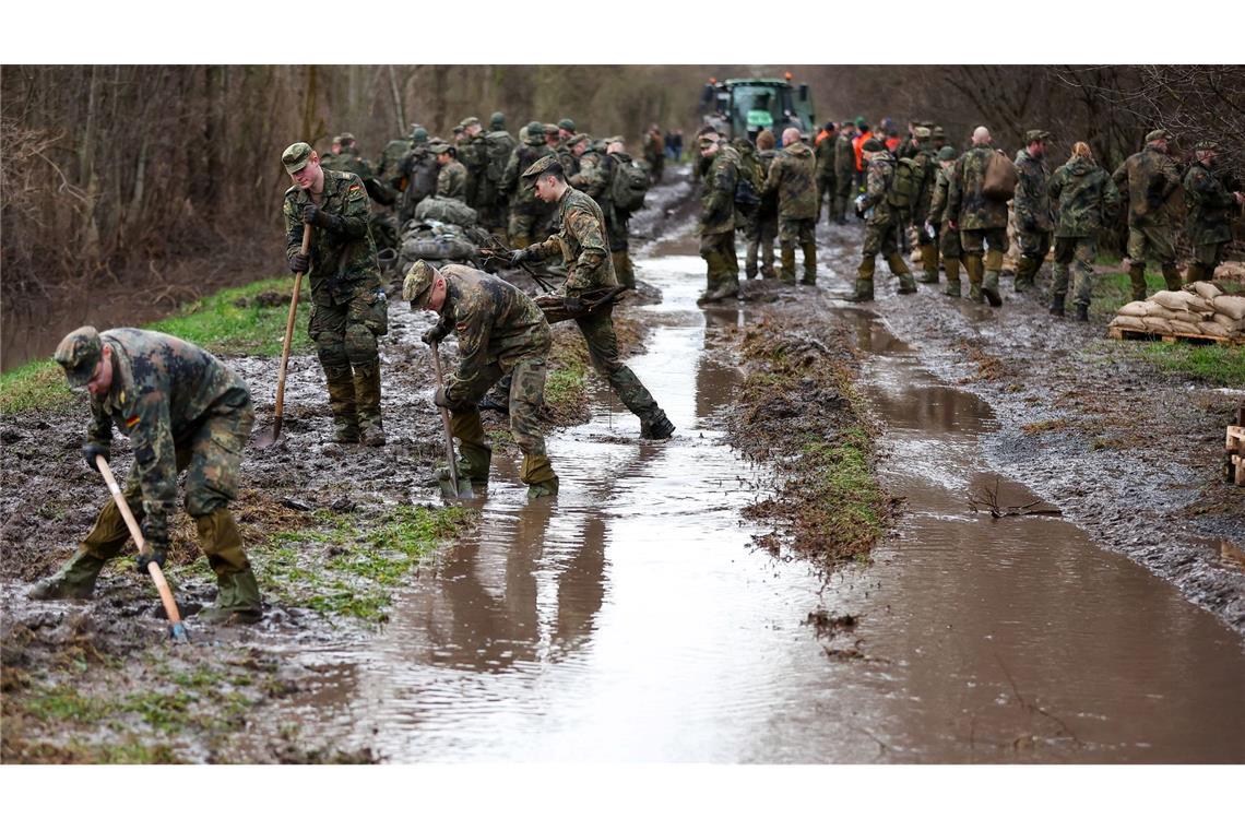 Soldatinnen und Soldaten der Bundeswehr sichern einen Deich an der Helme in Sachsen-Anhalt mit Sandsäcken.