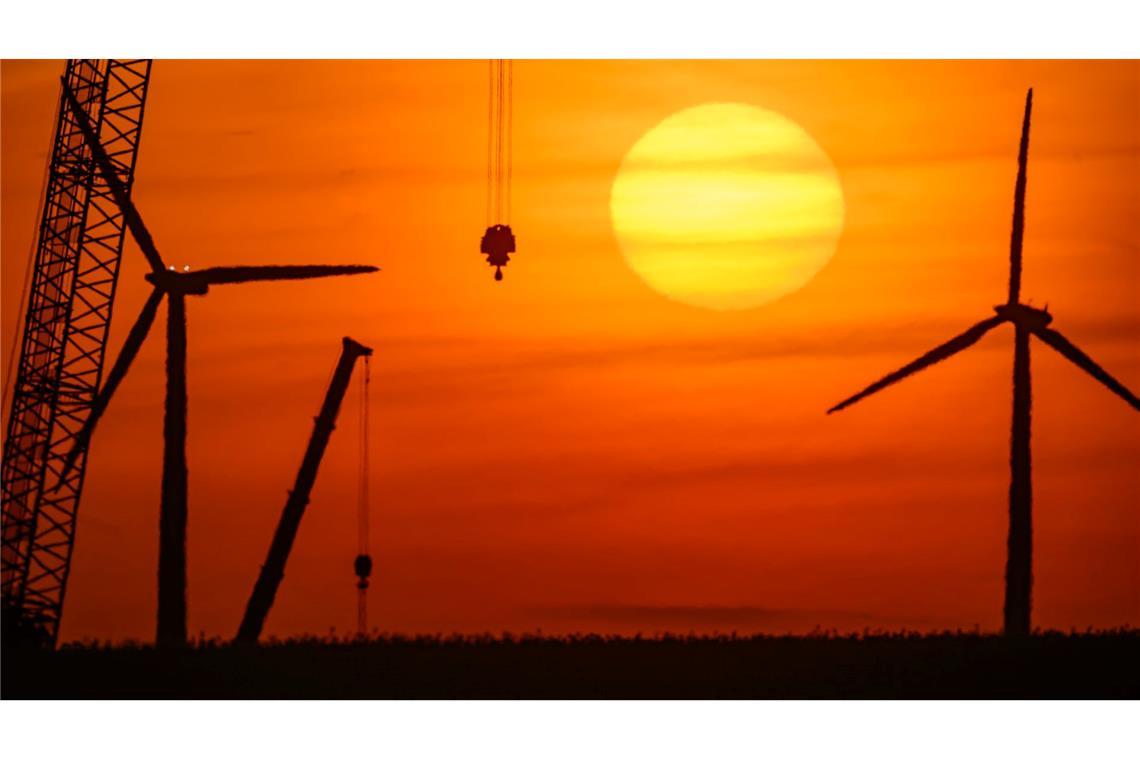 Bilder des Tages Sonnenaufgang über einer Landschaft mit Windenergieanlagen und einem Kran auf einer Baustelle für ein neues Windrad in Brandenburg.