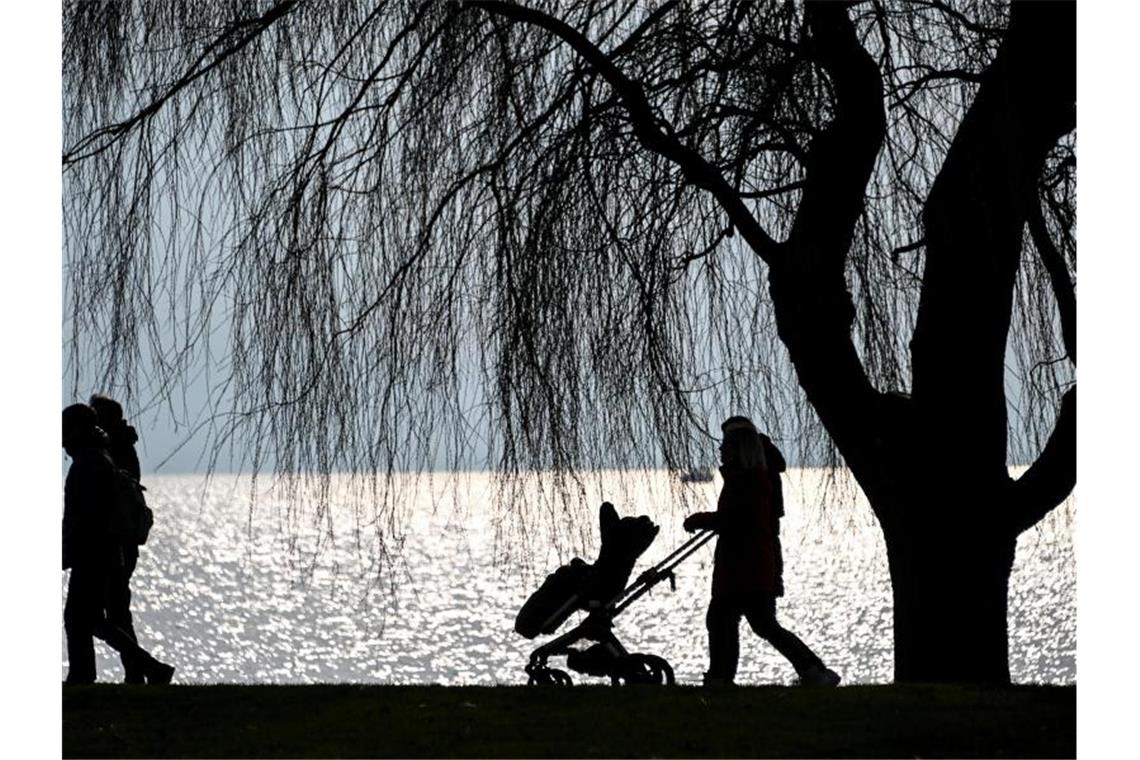 Spaziergänger gehen am späten Nachmittag am Ufer des Bodensees entlang. Foto: Felix Kästle/dpa