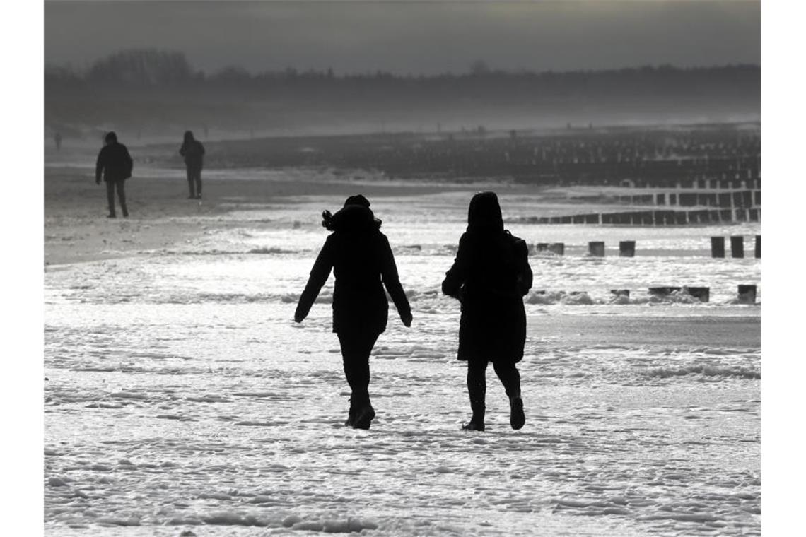 Spaziergänger laufen am Ostseestrand in Wustrow entlang - dort sorgte Sturmtief "Antonia" für dunklen Himmel und aufgeschäumtes Wasser. Foto: Bernd Wüstneck/dpa-Zentralbild/dpa