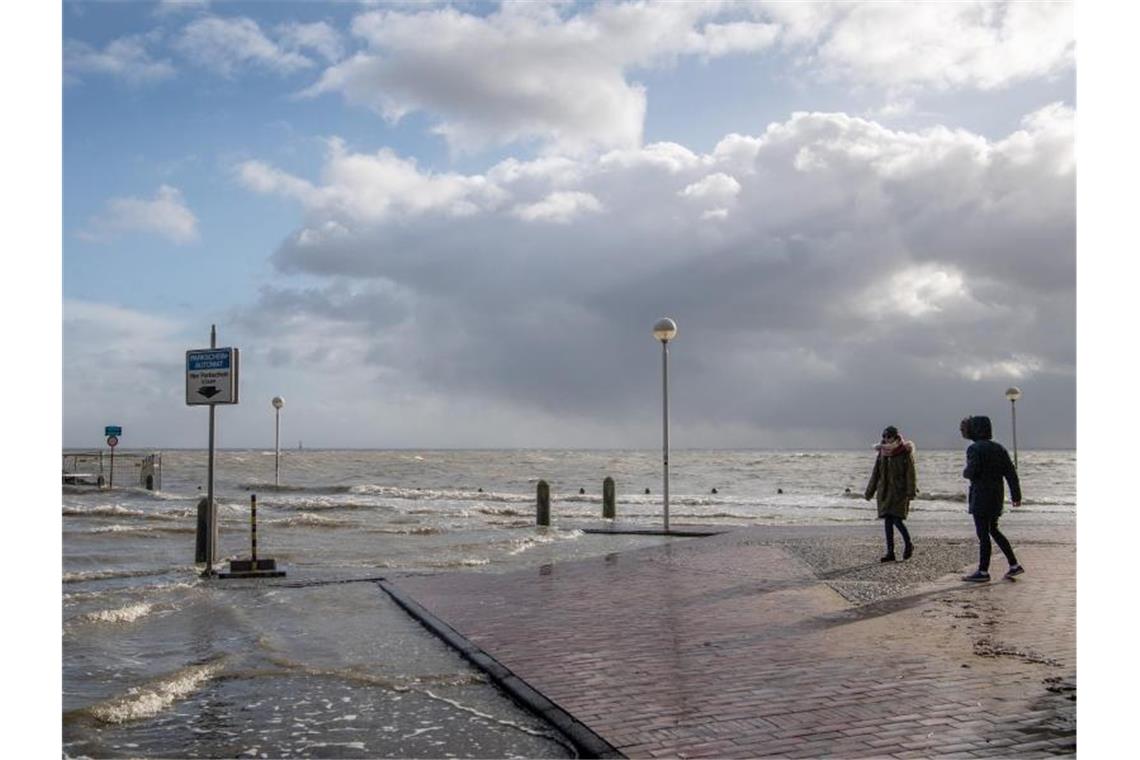 Spaziergänger laufen über einen überfluteten Parkplatz an der Nordseeküste. Foto: Sina Schuldt/dpa