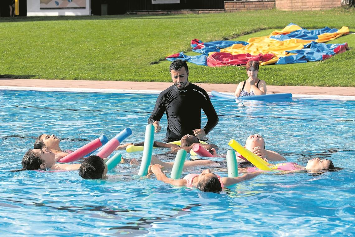 Spielerisch die Angst verlieren: Abdulfatt Wis zeigt den Kindern mit ihren Schwimmnudeln, wie die Haltung im Wasser sein sollte. Foto: J. Fiedler