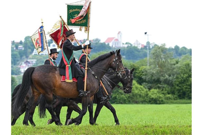 Standartenträger und Reiter aus Grünkraut reiten beim traditionellen „Blutritt“ einen Weg entlang. Foto: Felix Kästle/dpa/Archivbild