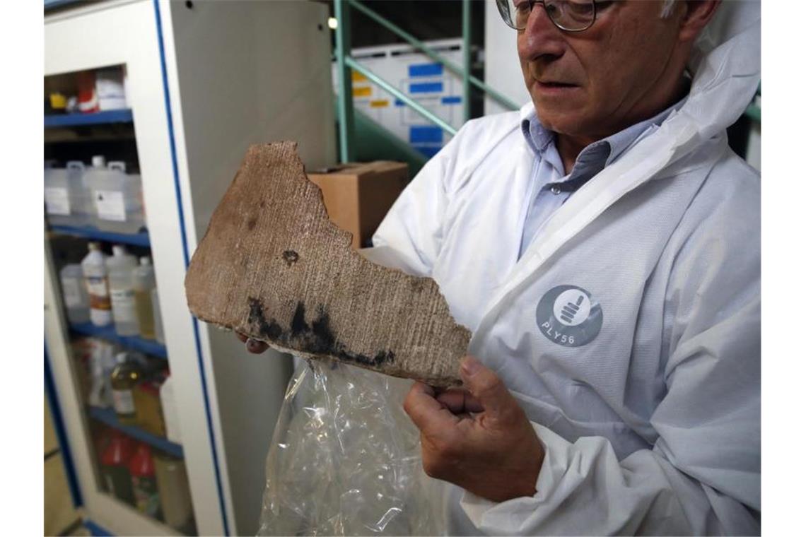 Steinspezialist Jean-Didier Mertz zeigt ein Fragment von verbranntem Stein. Foto: Francois Mori/AP/dpa