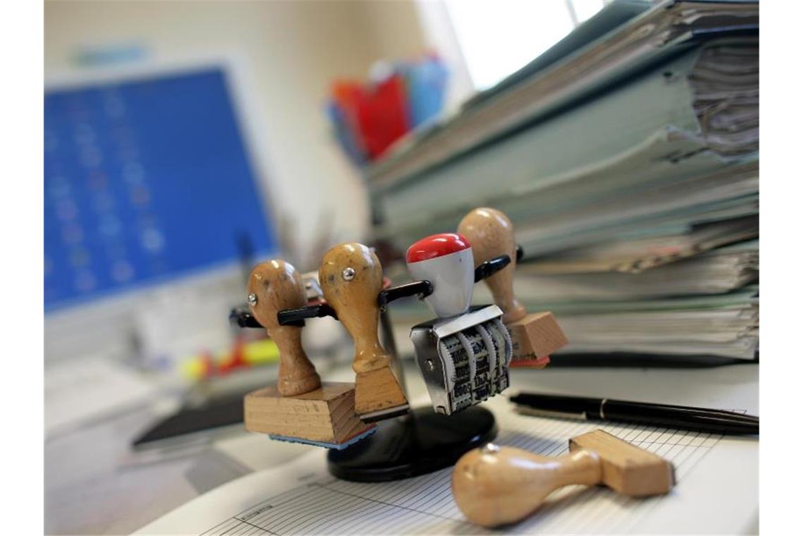 Stempel und Akten auf einem Schreibtisch. Die Industrie fordert die Lockerung von Fristvorgaben und Informationspflichten für Unternehmen. Foto: Patrick Pleul/dpa-Zentralbild/dpa