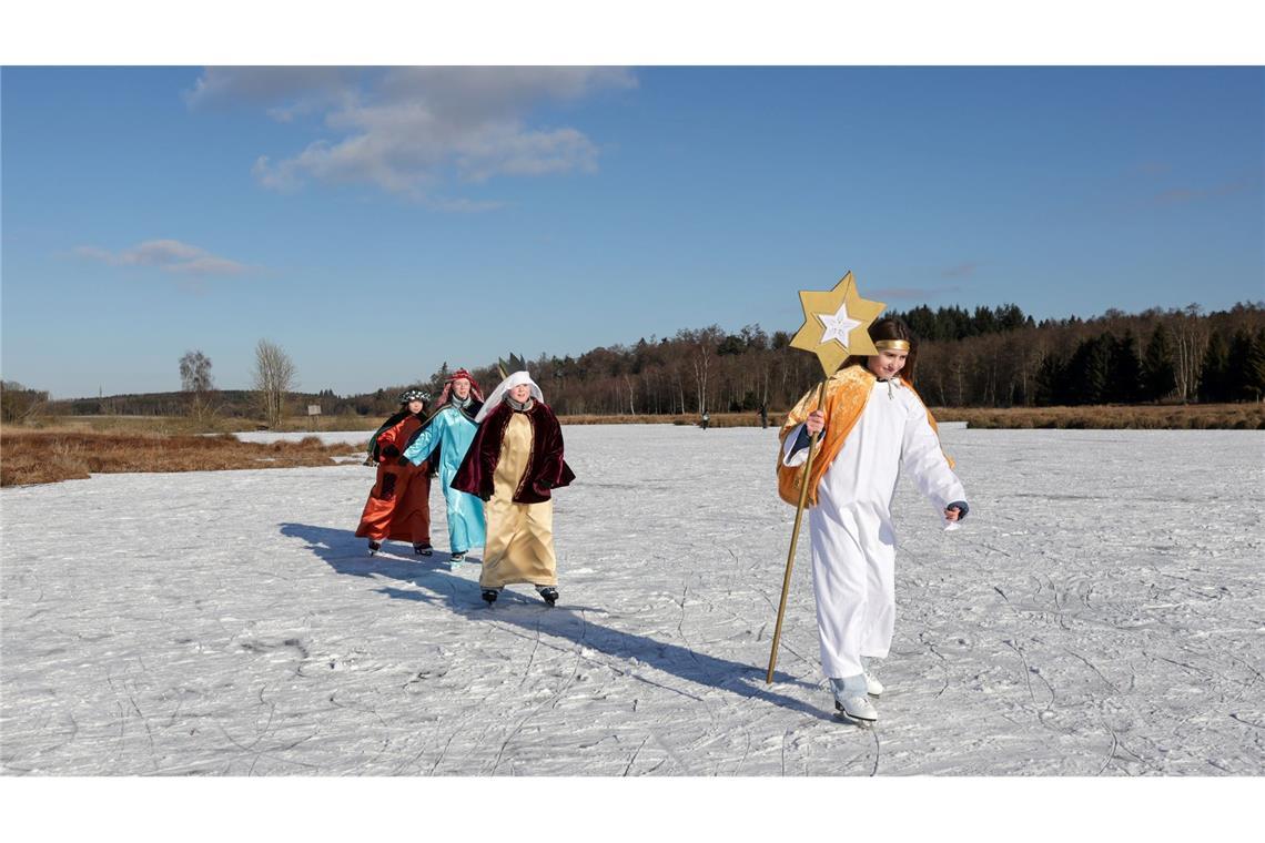 Sternsinger sind im Sonnenschein bei Betzenweiler in Tiefenbach mit Schlittschuhen auf einem zugefrorenen See unterwegs.