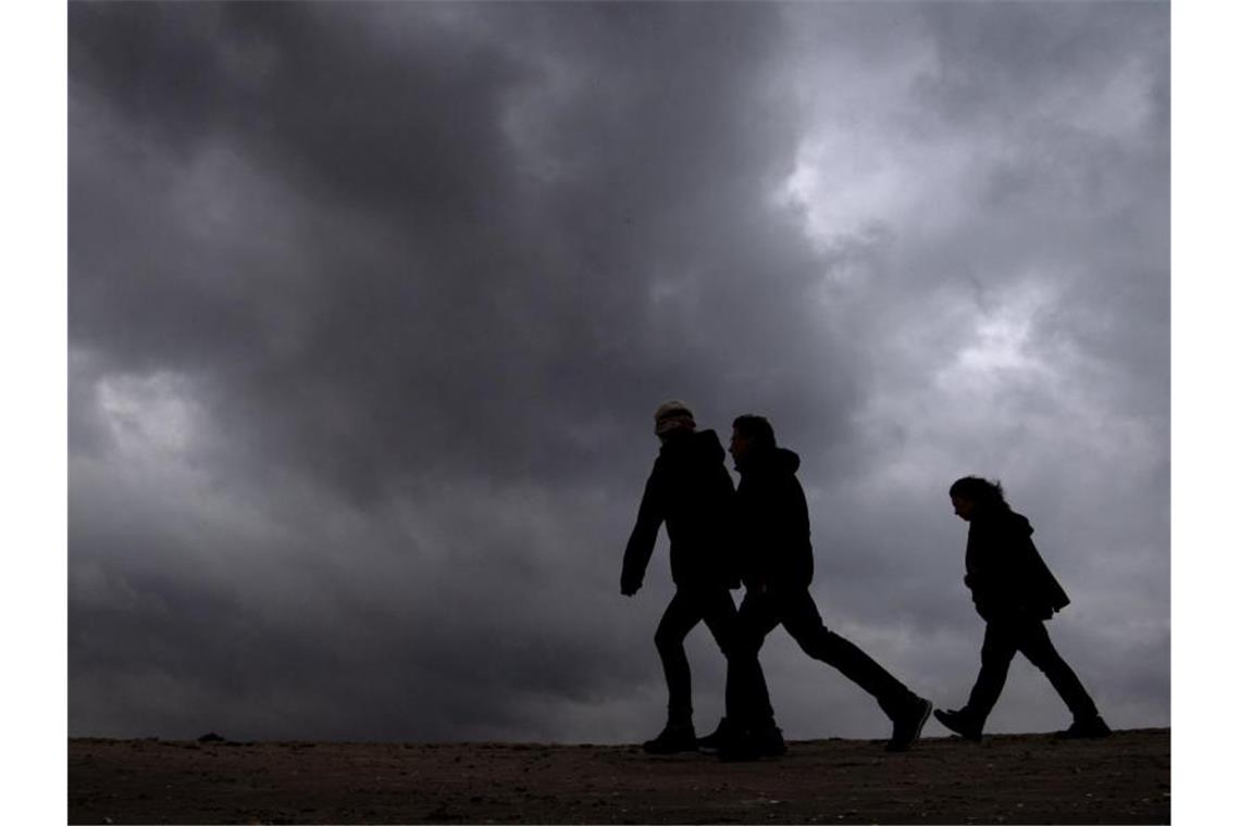 Strand-Spaziergänger unter dunklen Wolken. Foto: Sina Schuldt/dpa