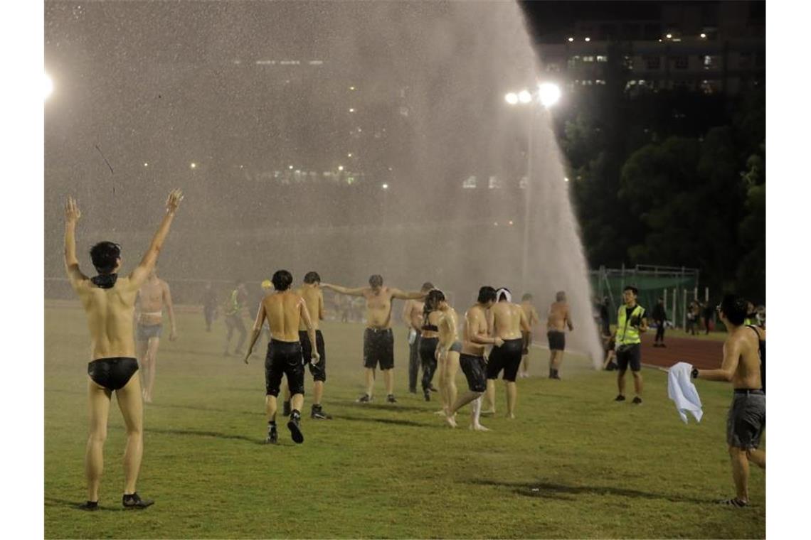 Studenten stehen bei Zusammenstößen mit der Polizei an der Chinese University unter dem Strahl eines Wasserwerfers. Foto: Kin Cheung/AP/dpa